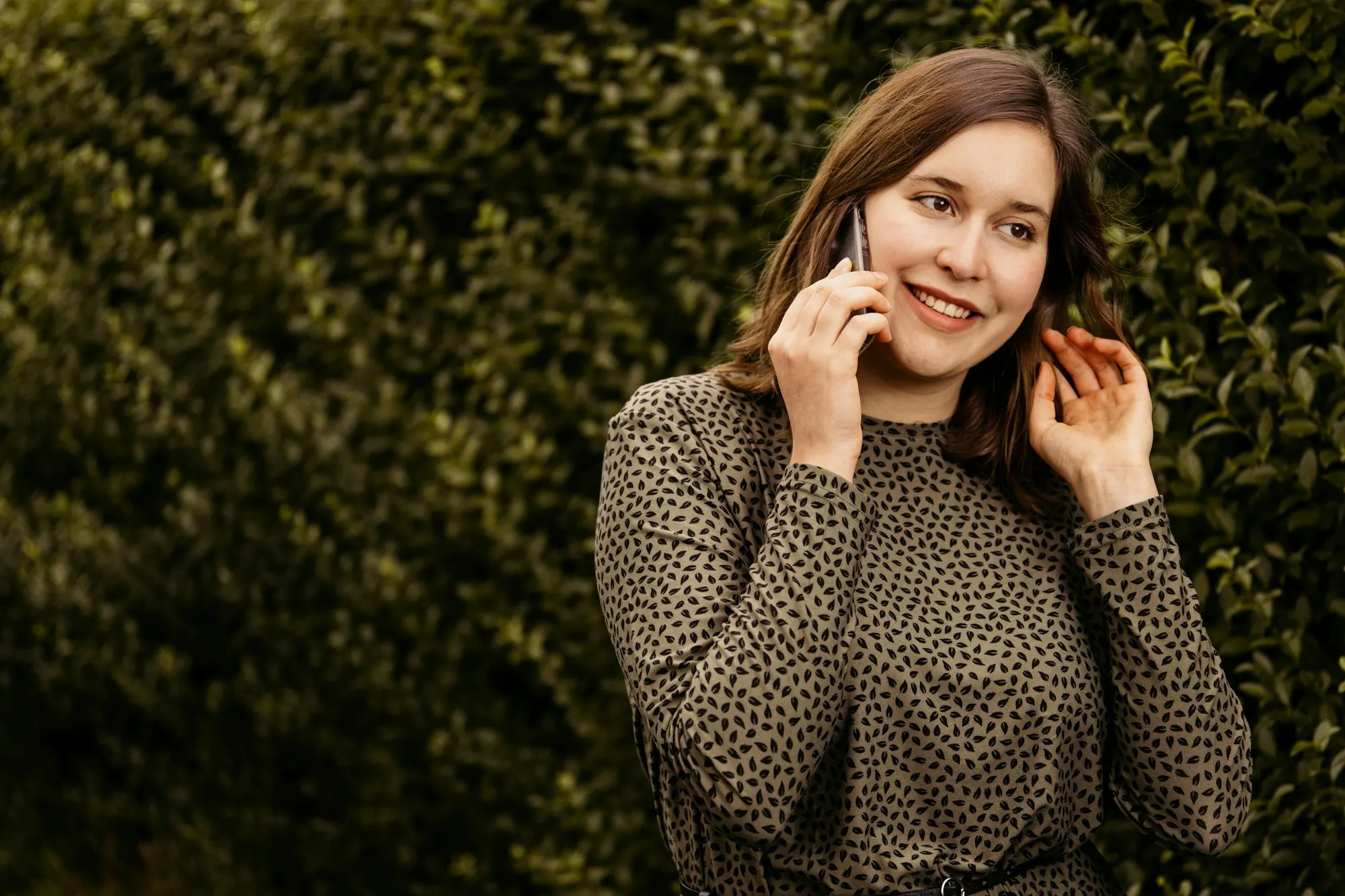 Uma mulher sorri ao falar ao telemóvel num jardim