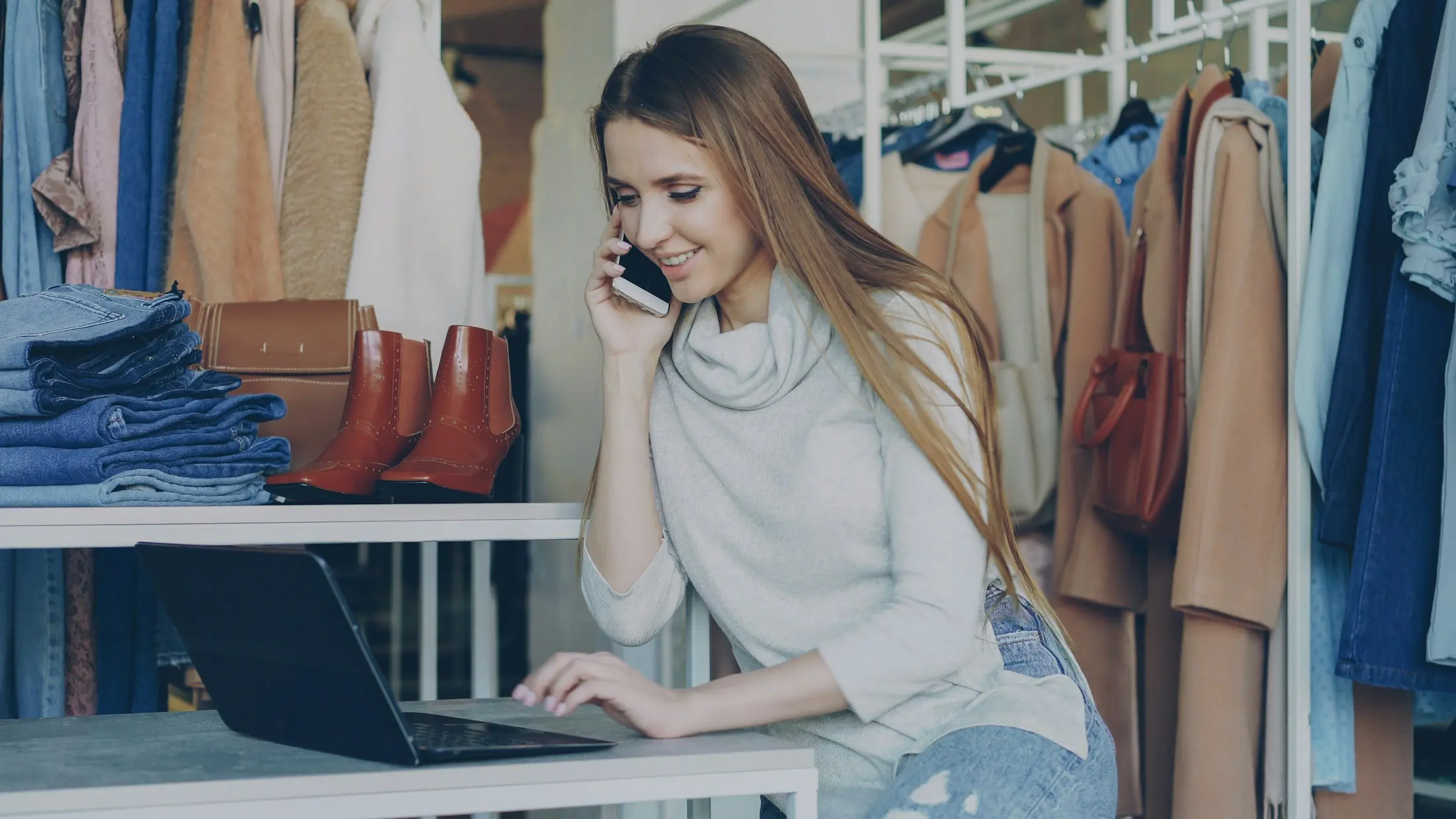 A dona de uma loja de roupa fala ao telefone, ao lado do portátil